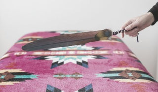 A feather clearing away energy over a massage table with a colorful blanket